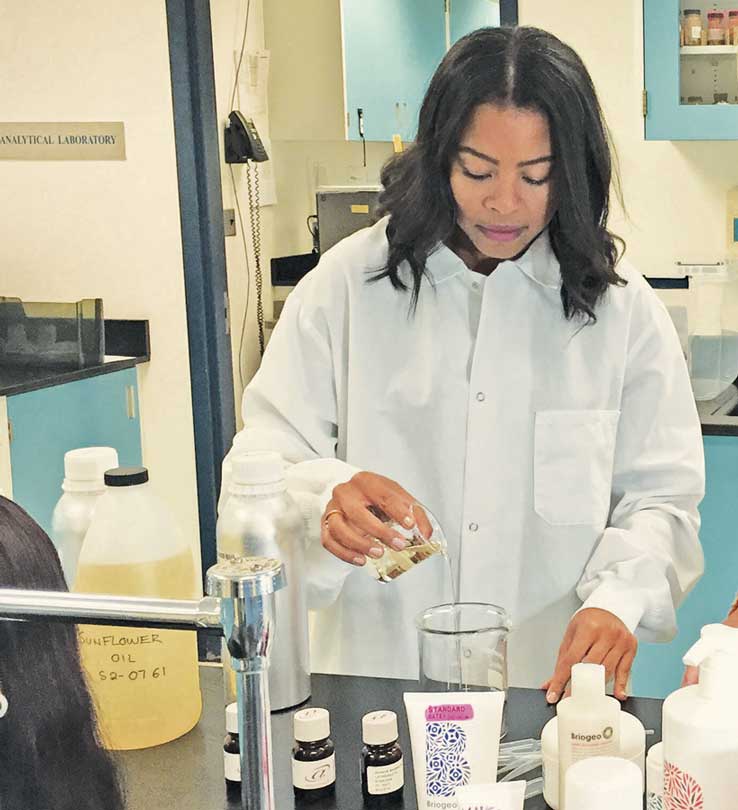 Briogeo founder Nancy Twine pours ingredients between beakers in a lab coat