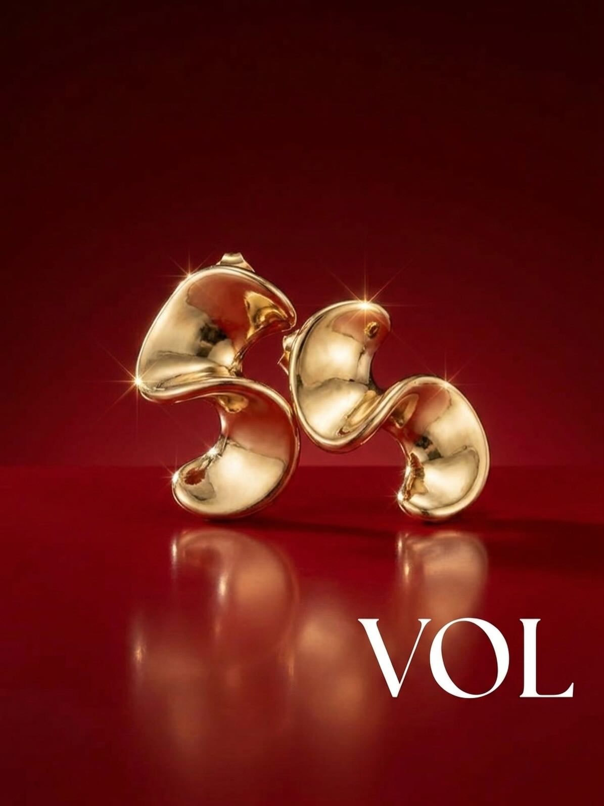Sculptural gold earrings against a deep red background